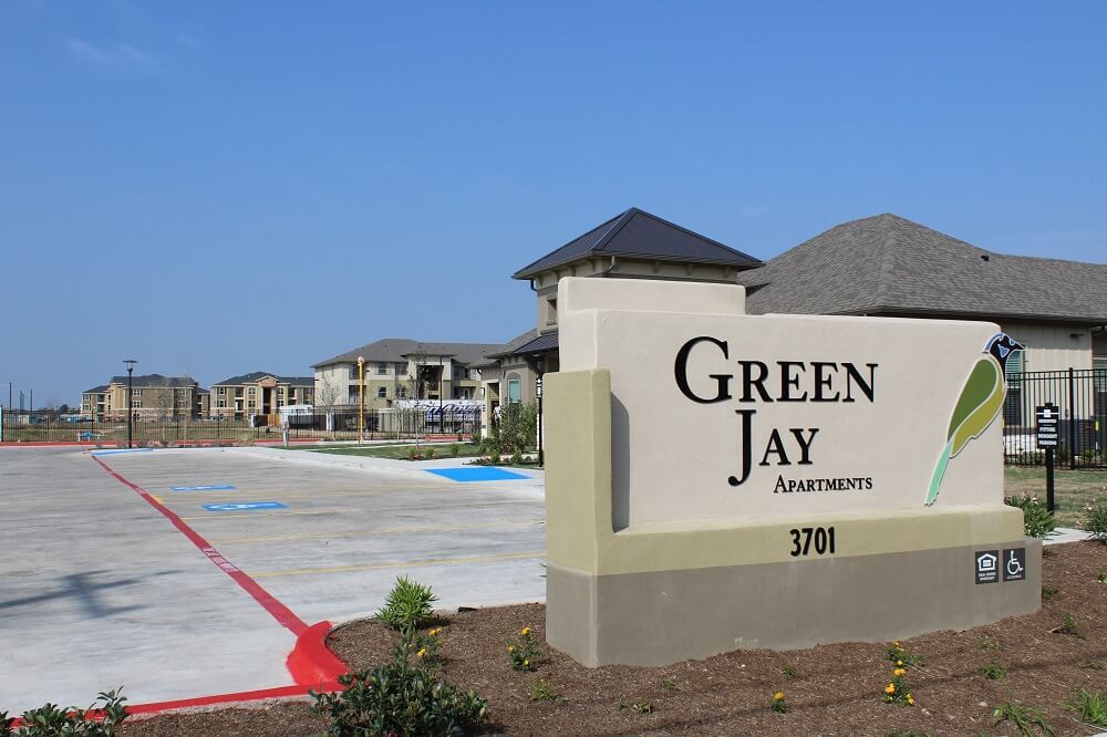 Monument sign in front of parking lot; reads Green Jay Apartments